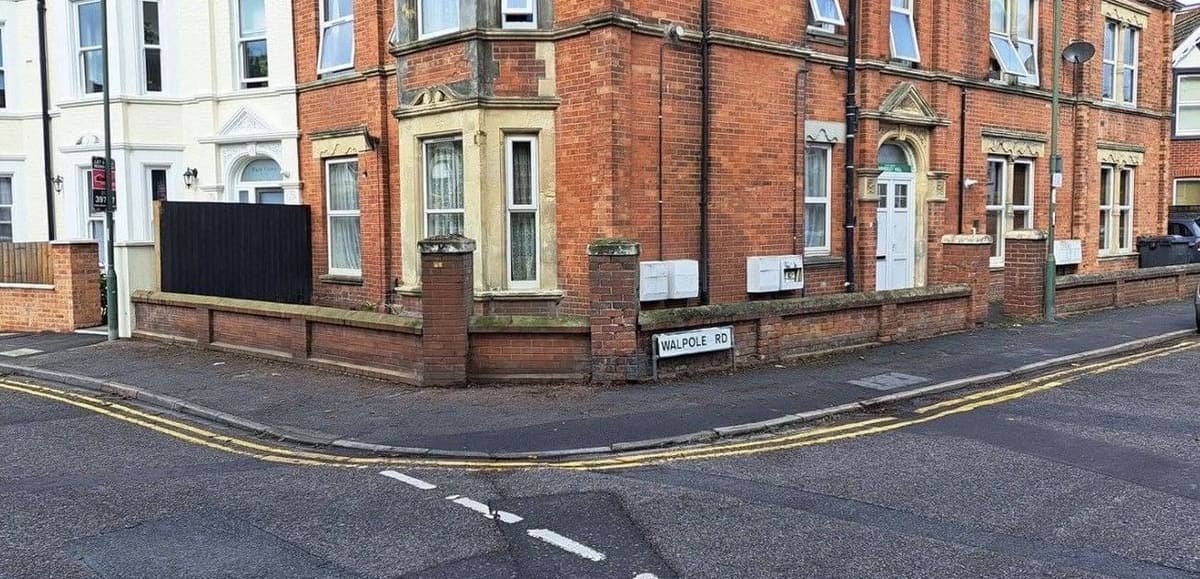 Corner plot with an overgrown hedge removed, revealing the brick wall and building frontage