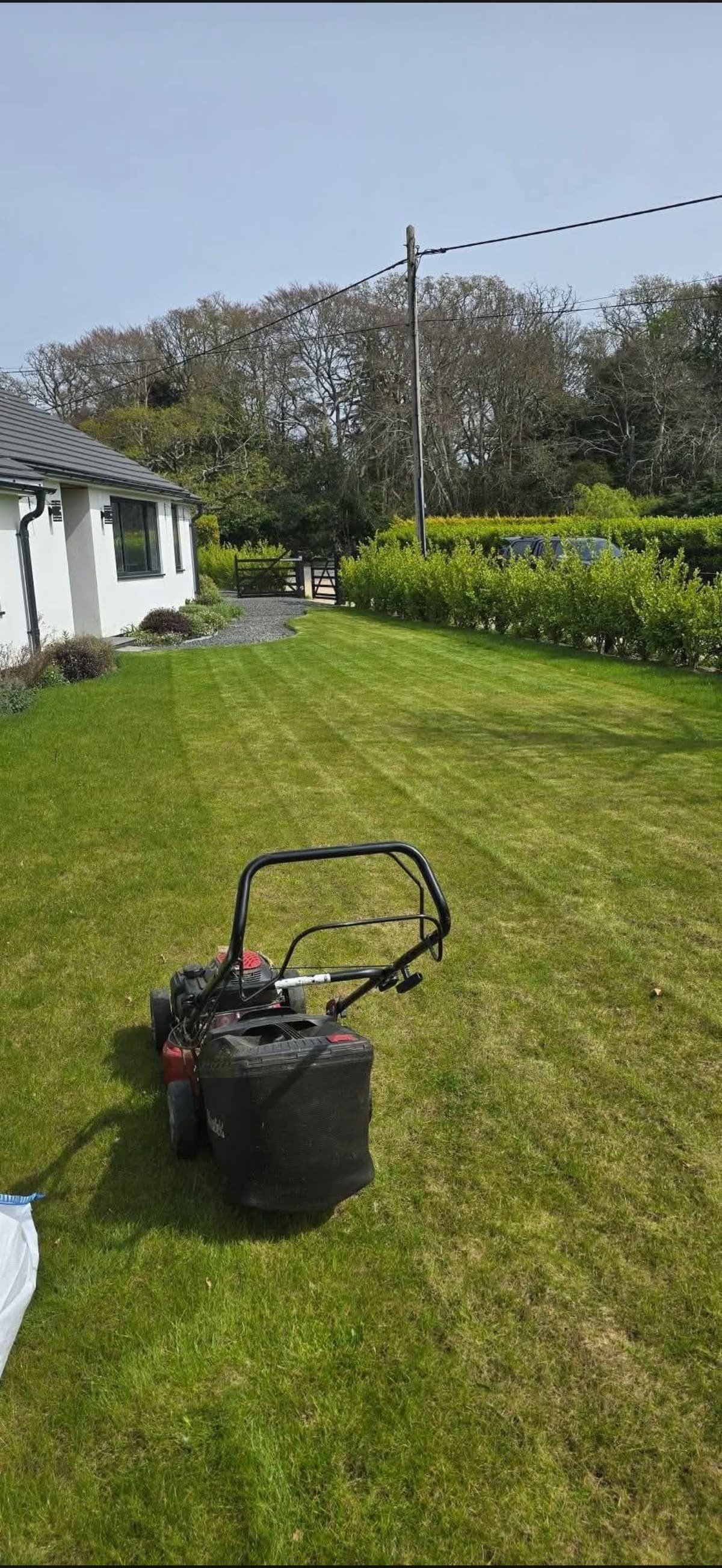 Lawn mower on a freshly striped lawn beside a white house and clipped hedge
